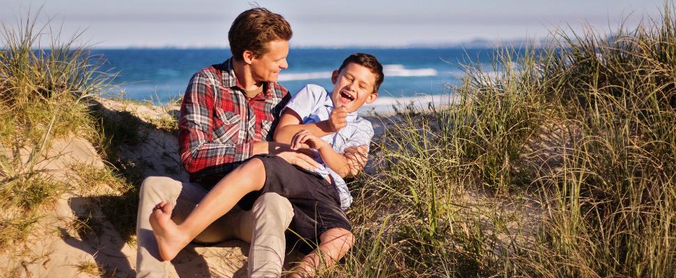 Man making teenage boy laugh on the beach