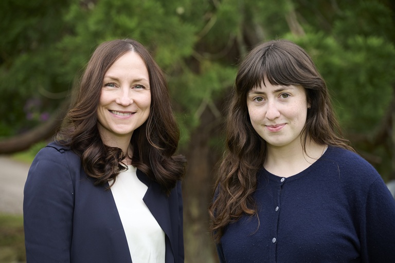 Two ladies standing together smiling.