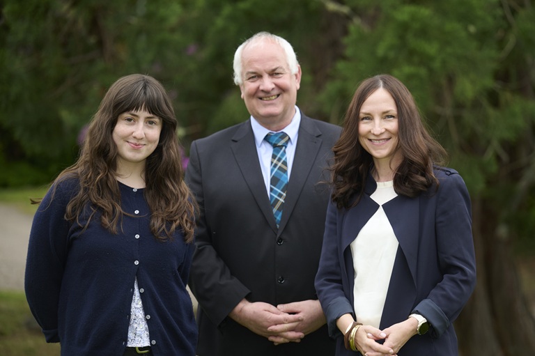Three people standing together, one man and two women, smiling.