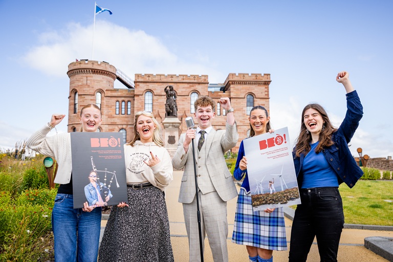 Five people standing in front of Inverness Castle, celebrating. They are holding two prints outs of the front and back page of the bid document.