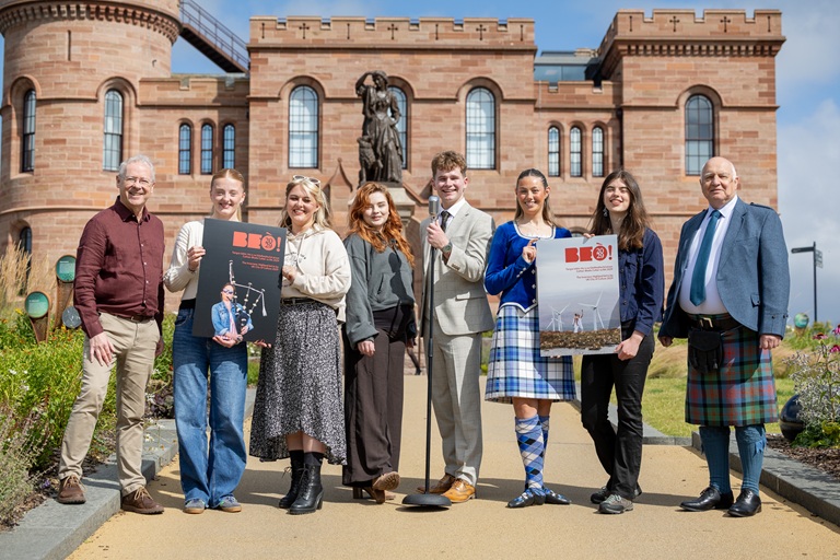 Eight people standing in front of Inverness Castle. Two are holding prints of the front and back page of the bid document.